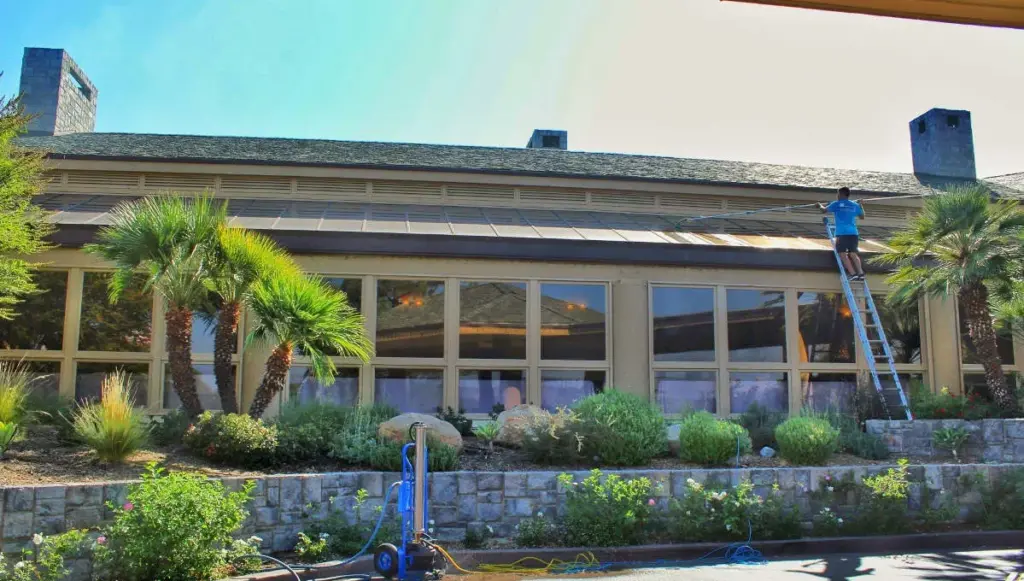 A professional performing roof cleaning on a commercial building, removing dirt and grime.